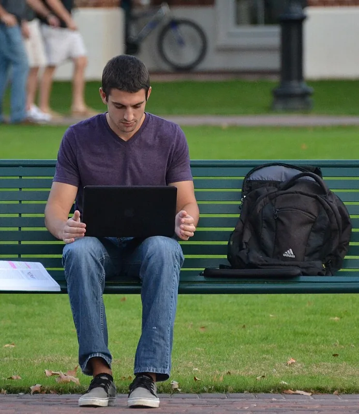 A student working on a laptop on a campus bench