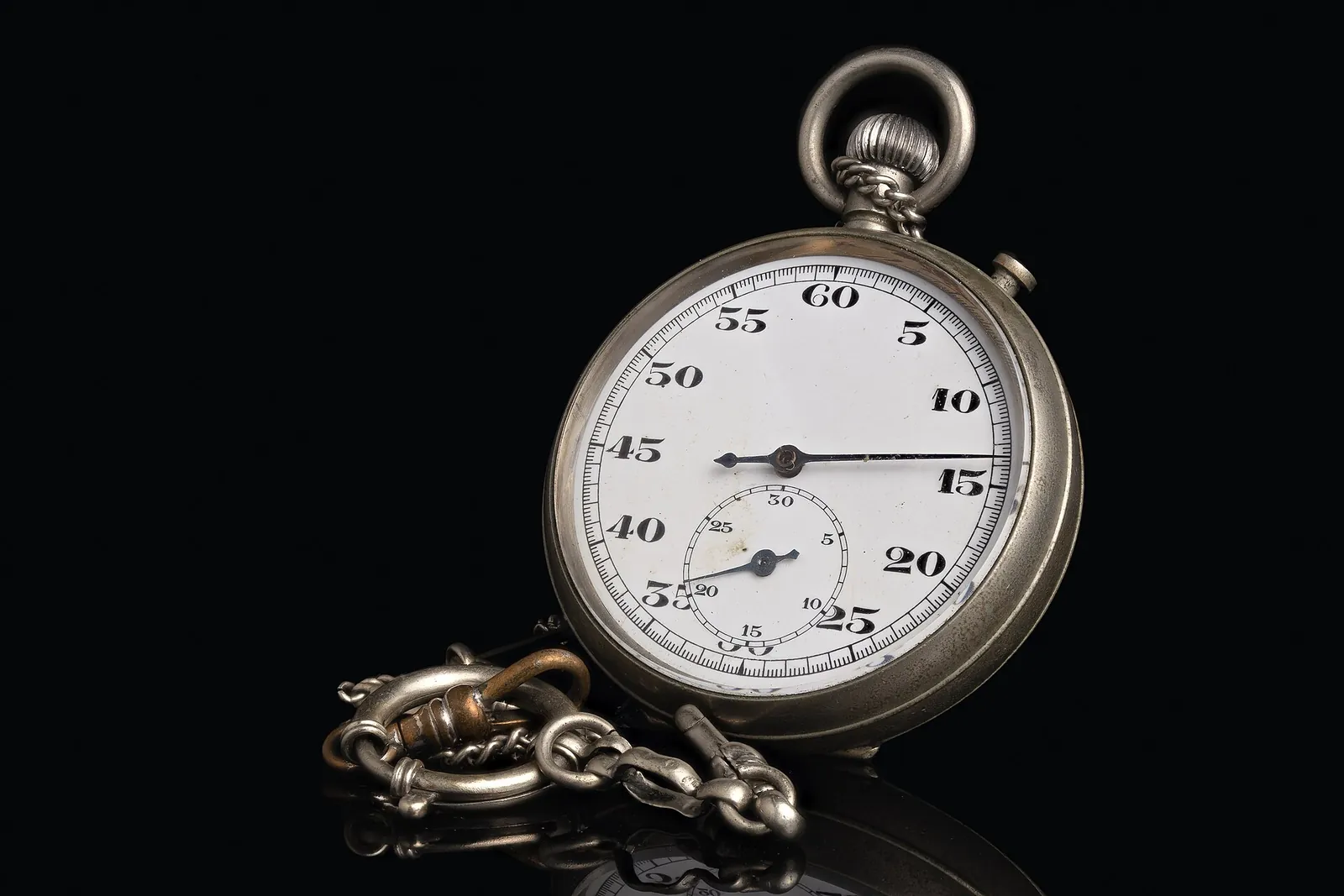 An old silver pocket stopwatch with a white dial and a metal chain, on a black background